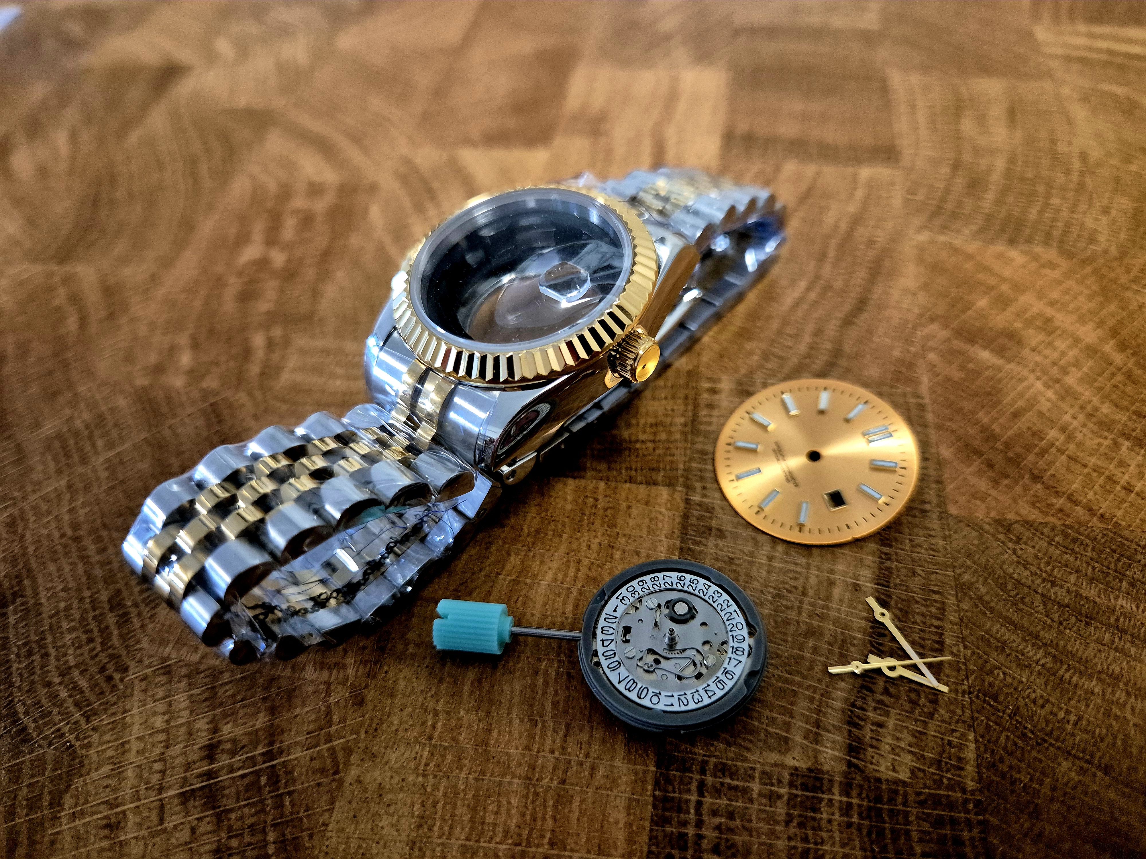 An NH05 automatic movement laid out next to the case, dial, hands, and bracelet — ready for assembly