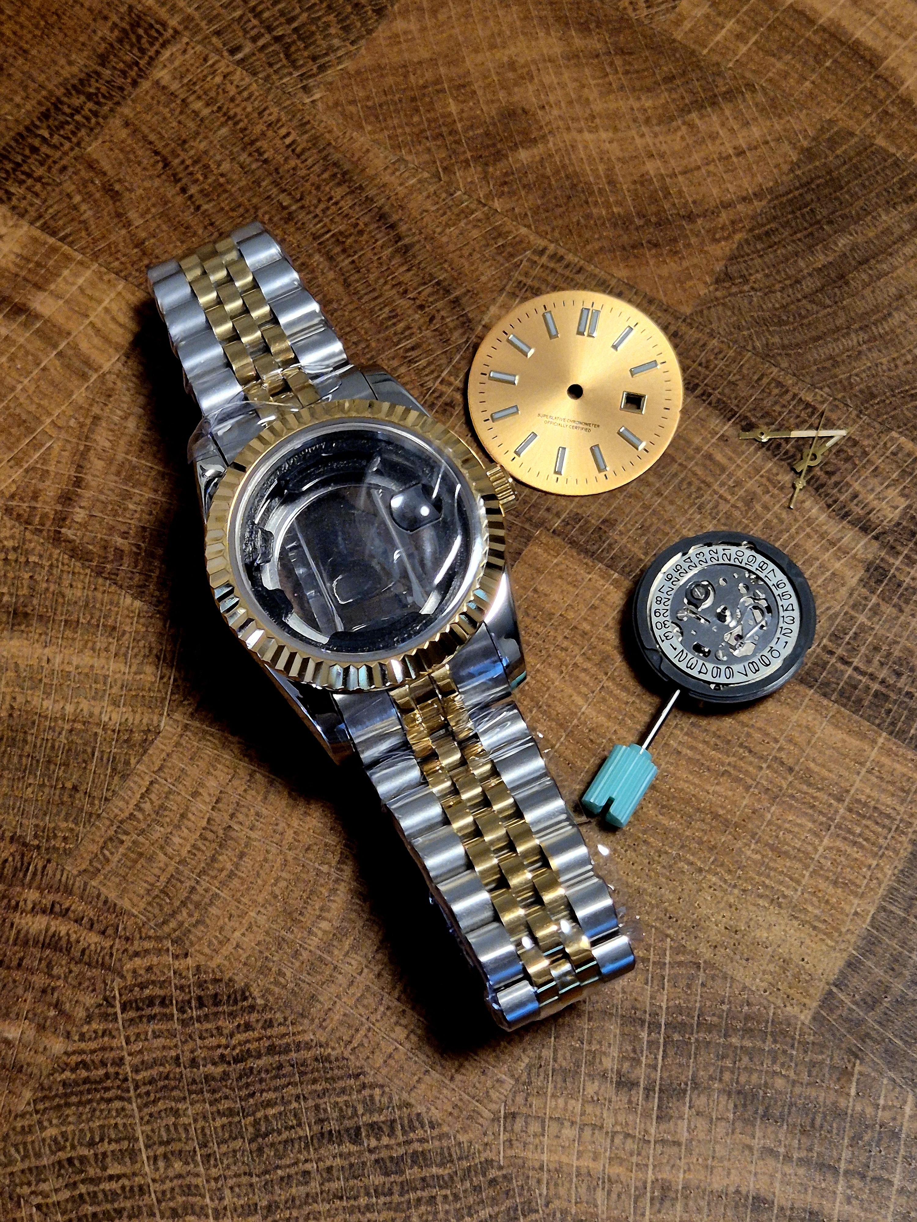 A Seiko NH05 movement laid out alongside the case, dial, hands, and bracelet — the bare movement and date wheel visible in the foreground