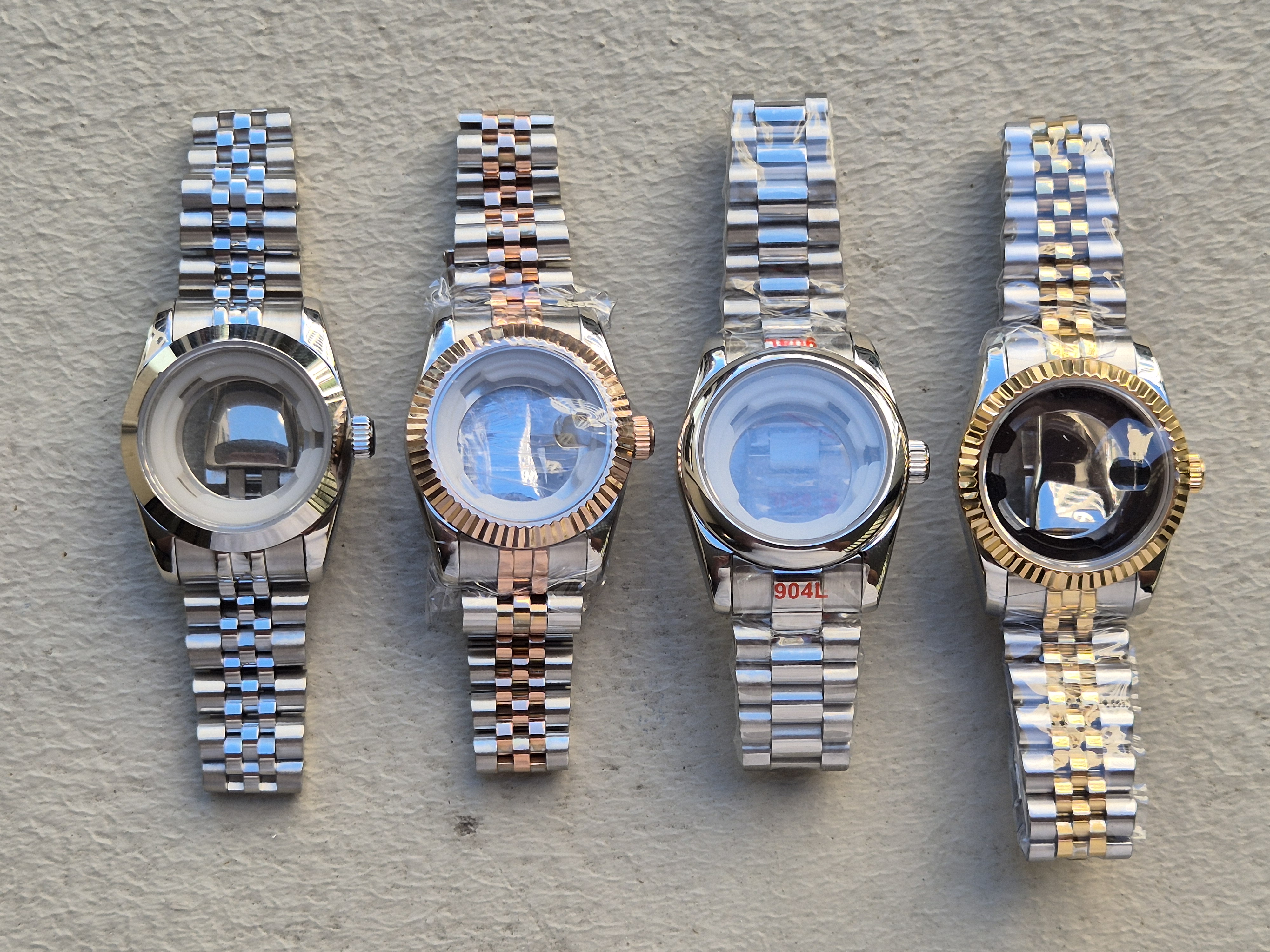 Four Jubilee cases laid out on a workbench — two-tone gold, polished steel, two-tone rose gold, and stainless